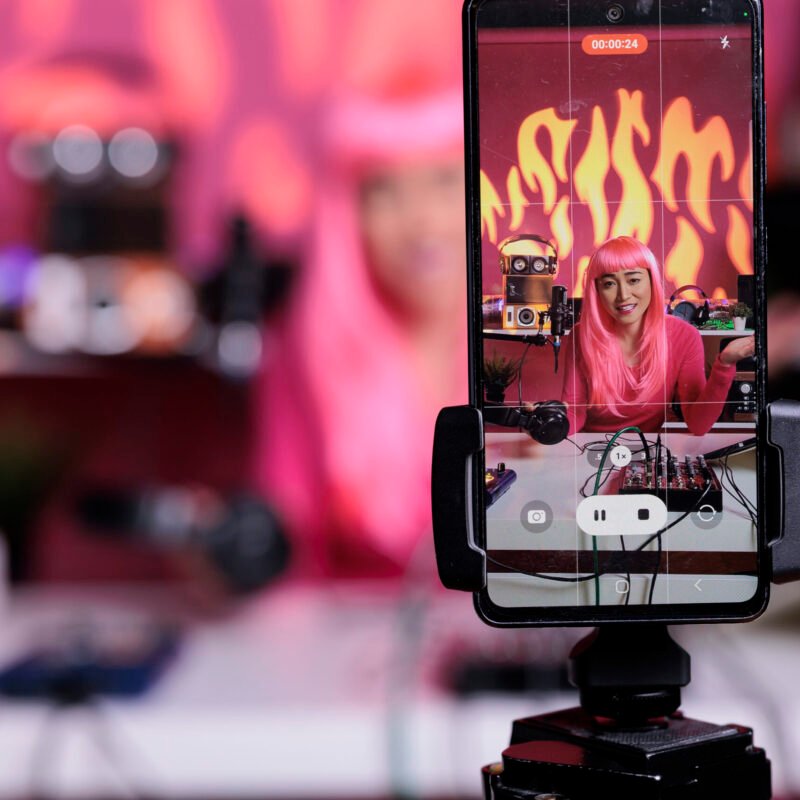 Influencer recording podcast using professional vlogging equipment while standing in streaming studio, posting vlog on social media to gain subscribers. Asian creator filming vlog with phone camera