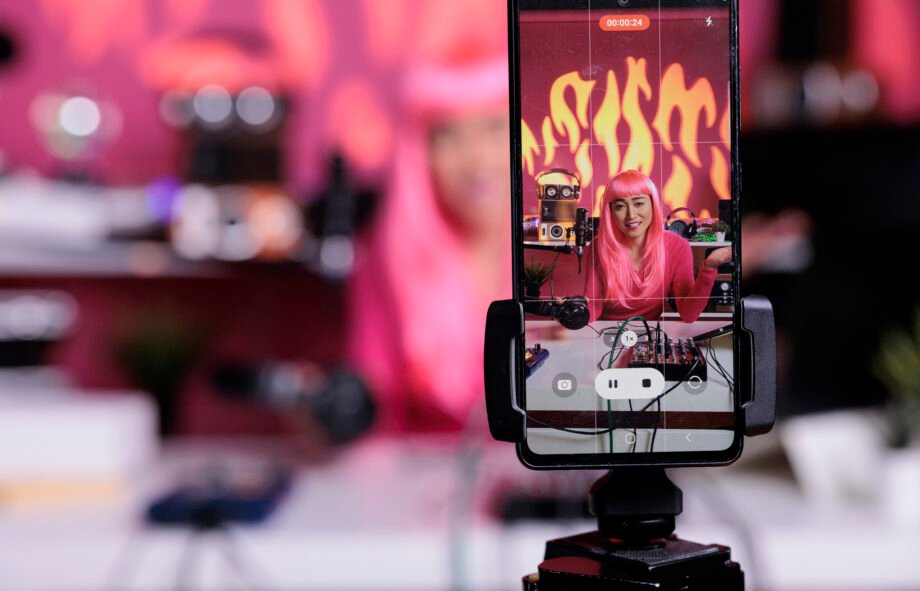 Influencer recording podcast using professional vlogging equipment while standing in streaming studio, posting vlog on social media to gain subscribers. Asian creator filming vlog with phone camera